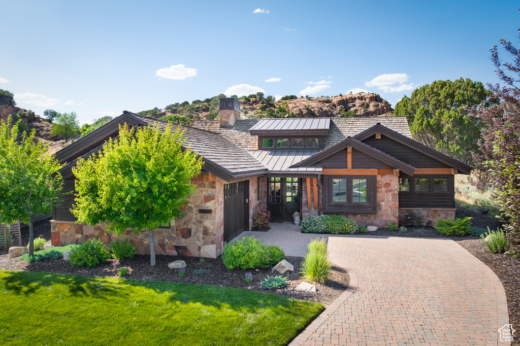View of front of house featuring stone siding, a chimney, a front yard, and driveway