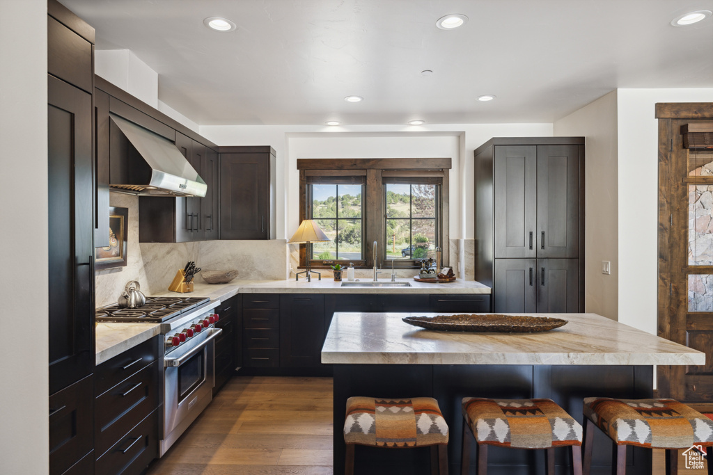 Kitchen with luxury range, wall chimney exhaust hood, a kitchen bar, recessed lighting, and tasteful backsplash