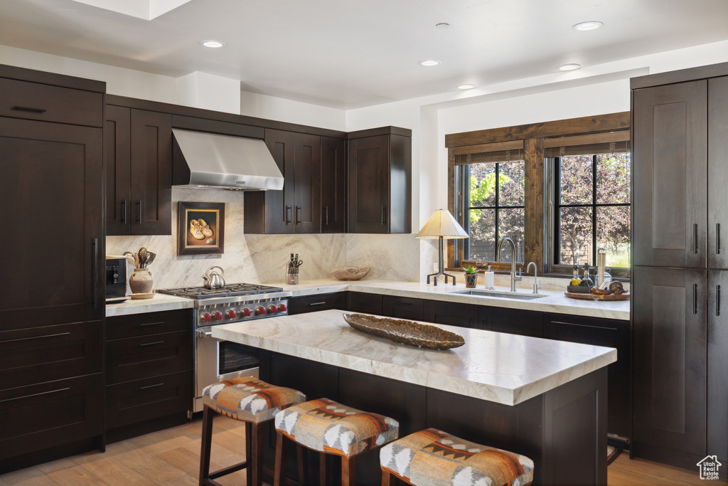 Kitchen with luxury stove, range hood, a kitchen bar, light countertops, and light wood-type flooring
