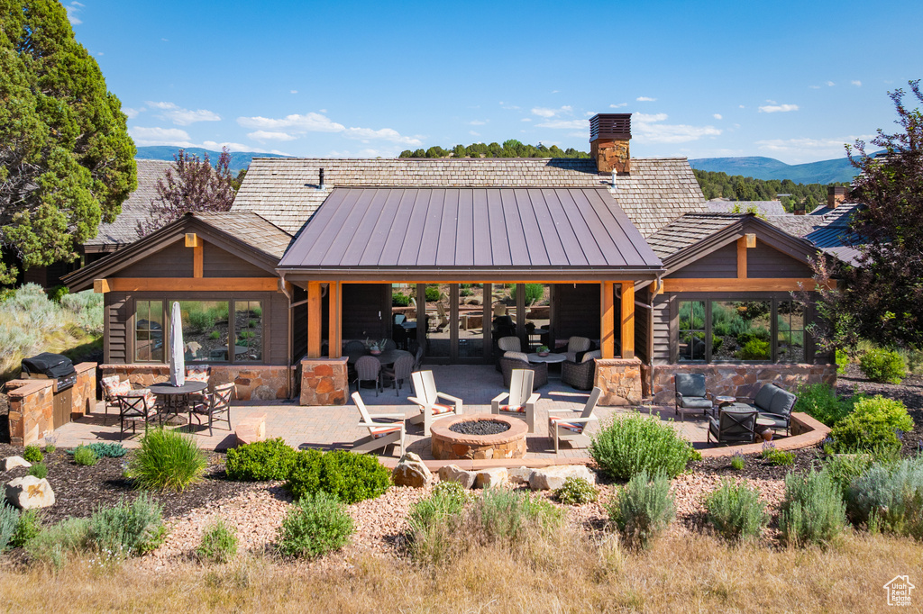 Rear view of property featuring an outdoor living space with a fire pit, a patio area, a standing seam roof, and a mountain view