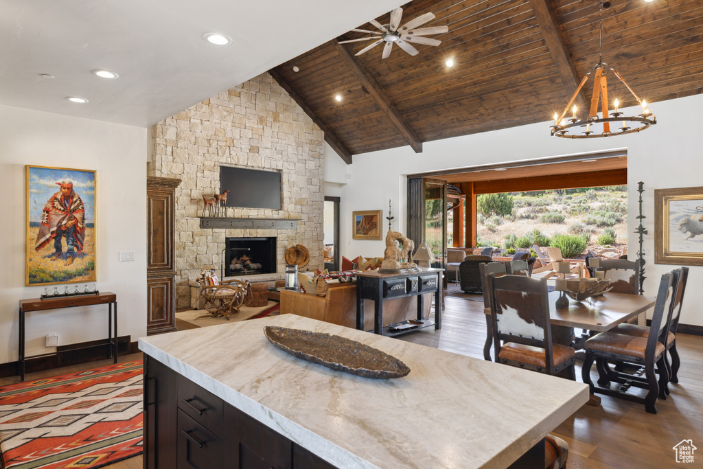 Dining space featuring wood finished floors, a stone fireplace, a chandelier, a ceiling fan, and high vaulted ceiling