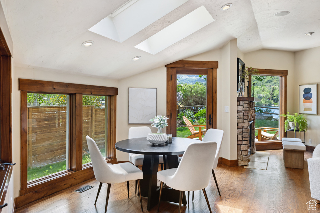 Dining space featuring a skylight, lofted ceiling, wood finished floors, a stone fireplace, and recessed lighting