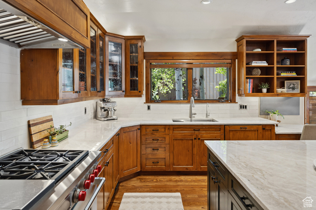 Kitchen featuring wall chimney exhaust hood, light wood-style flooring, backsplash, light stone counters, and recessed lighting