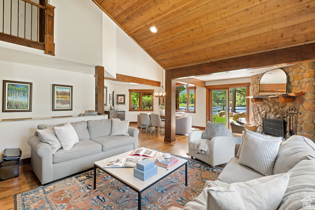 Living area with a chandelier, hardwood / wood-style flooring, high vaulted ceiling, wooden ceiling, and a stone fireplace