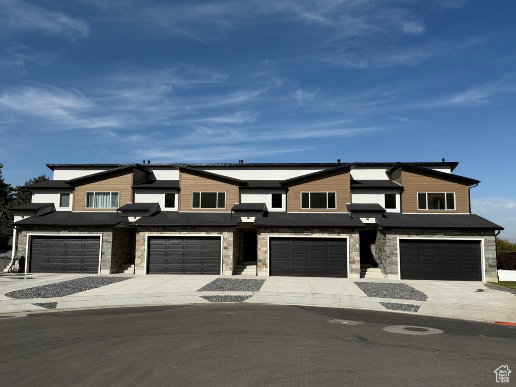 View of front of property featuring stone siding, an attached garage, and driveway