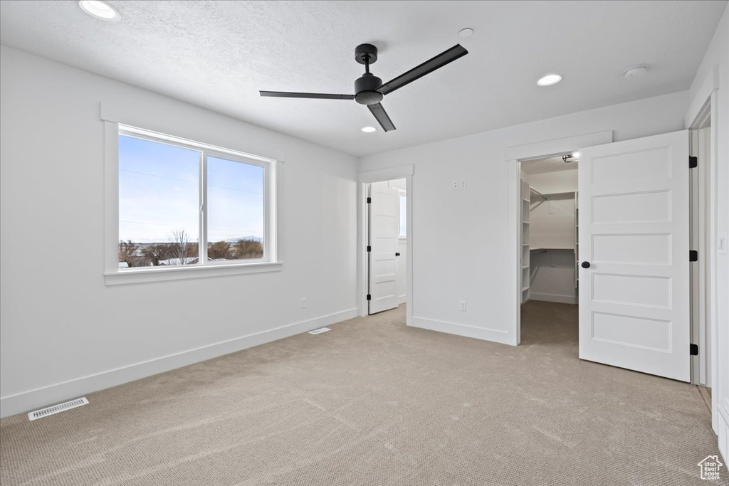 Unfurnished bedroom with light colored carpet, a spacious closet, recessed lighting, a closet, and a ceiling fan