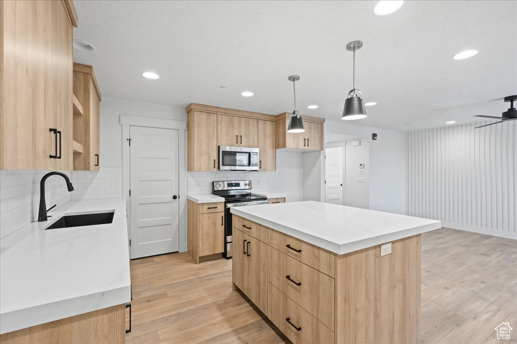 Kitchen with stainless steel appliances, light brown cabinets, light wood-style floors, decorative backsplash, and light countertops