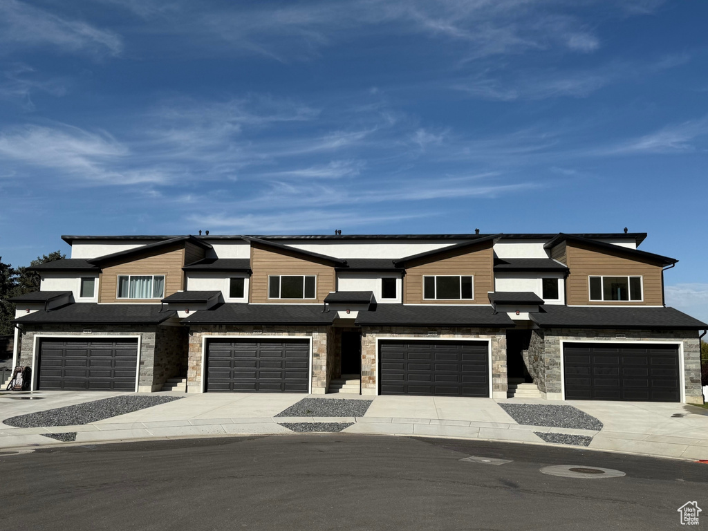 View of front of property featuring stone siding, an attached garage, and driveway
