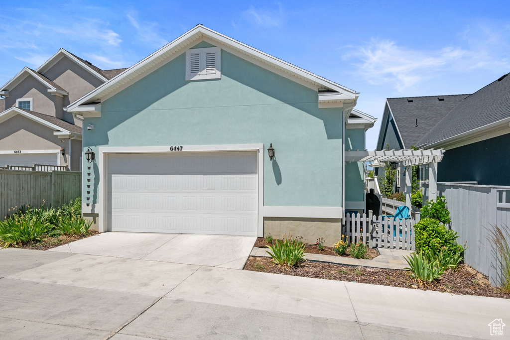 View of front facade featuring a garage, a pergola, stucco siding, and driveway