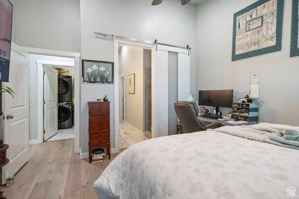 Bedroom featuring estacked washer and dryer, a barn door, light wood-style flooring, a towering ceiling, and a desk