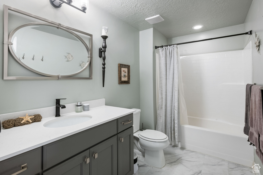 Bathroom featuring vanity, shower / bath combination with curtain, a textured ceiling, and marble finish flooring
