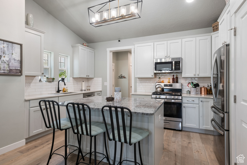 Kitchen with stainless steel appliances, a kitchen island, decorative backsplash, light wood-style floors, and a kitchen bar