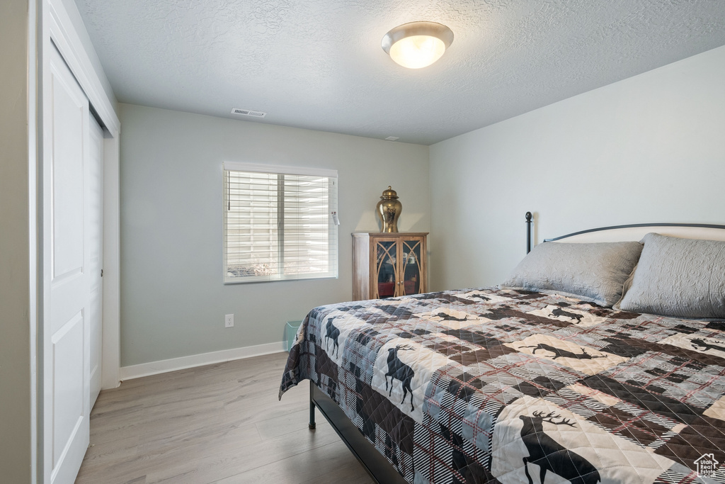 Bedroom with light wood-style flooring, a closet, and a textured ceiling
