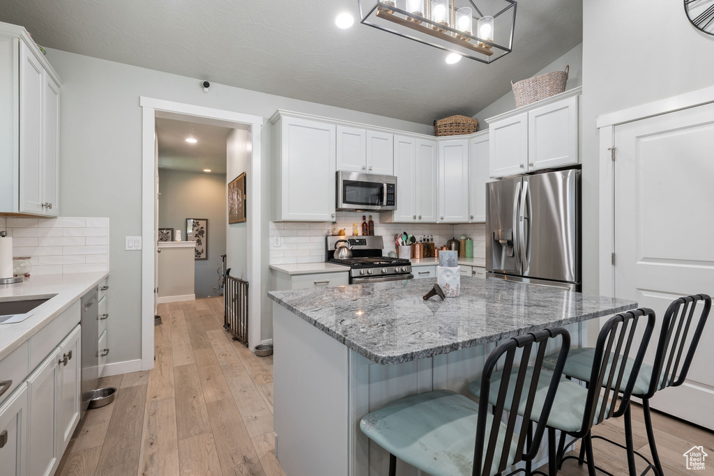 Kitchen featuring appliances with stainless steel finishes, a kitchen breakfast bar, white cabinetry, and recessed lighting