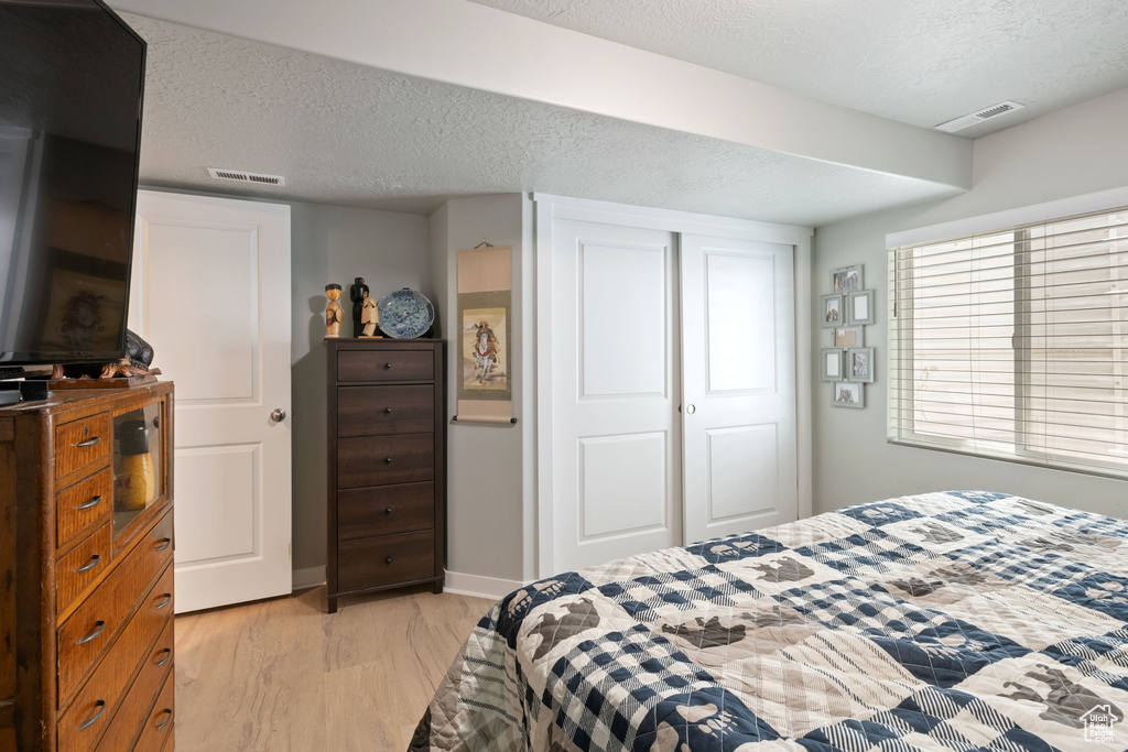 Bedroom featuring light wood-type flooring, a textured ceiling, and a closet