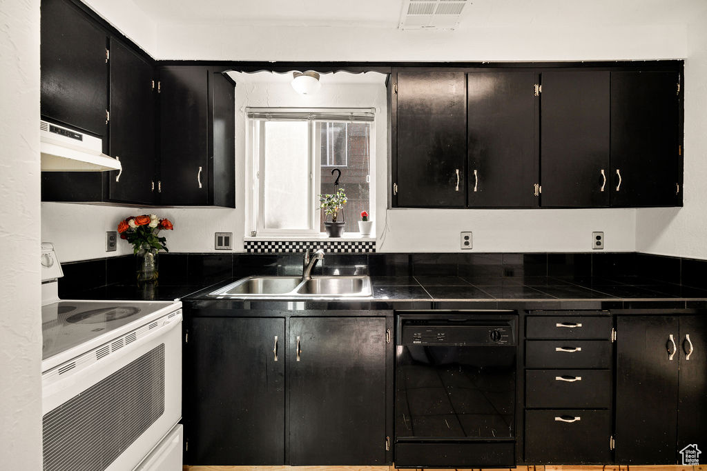 Kitchen featuring dishwasher, under cabinet range hood, white range with electric stovetop, and dark cabinetry