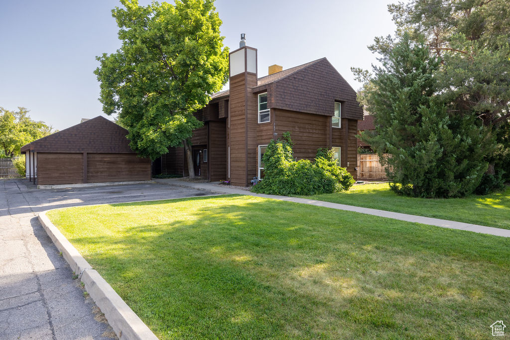 View of front of home featuring a garage, a chimney, a shingled roof, and an outbuilding