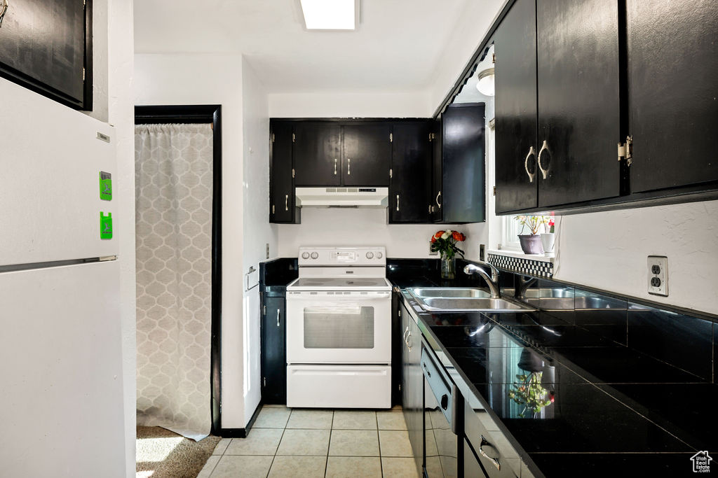 Kitchen with white appliances, under cabinet range hood, dark cabinets, and light tile patterned floors