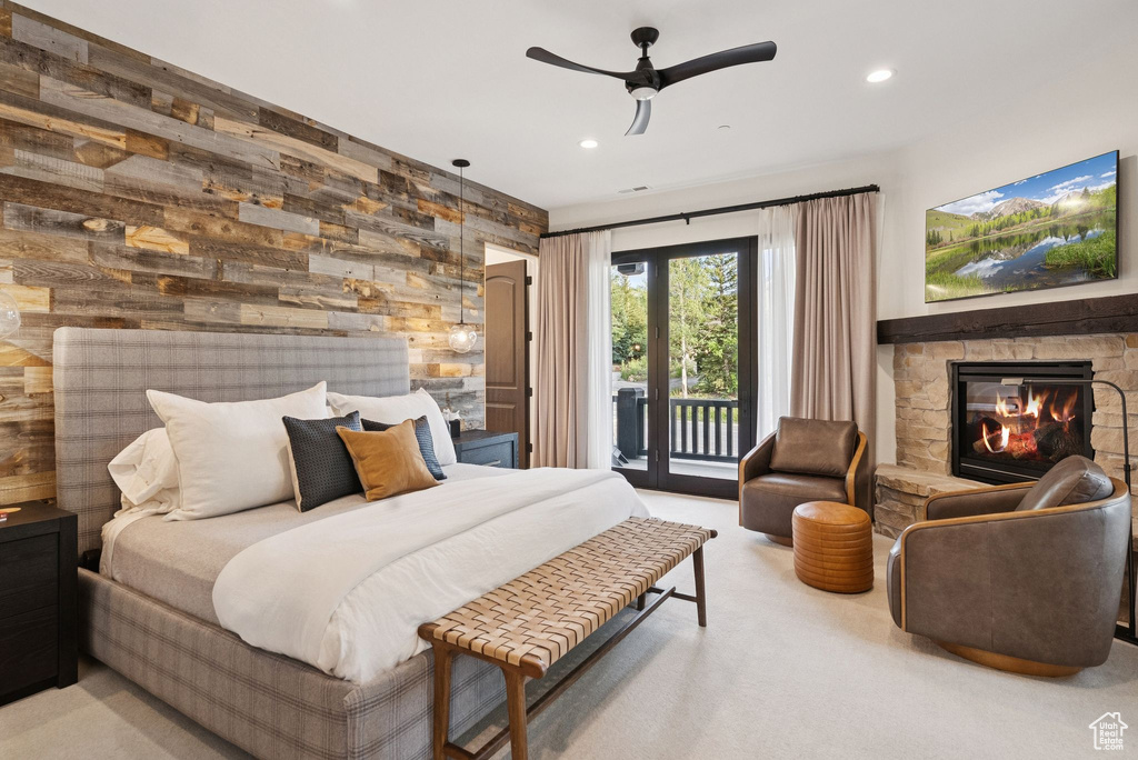 Carpeted bedroom with access to outside, a stone fireplace, wood walls, recessed lighting, and ceiling fan