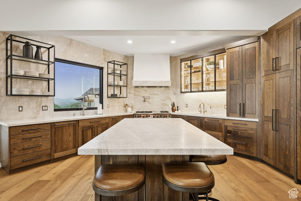 Kitchen featuring custom range hood, decorative backsplash, light countertops, a kitchen island, and light wood-type flooring