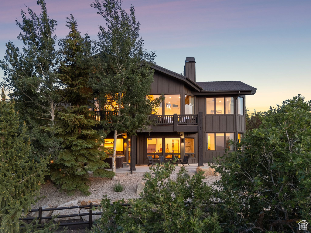 Back of property at dusk featuring a chimney, a patio area, and a deck