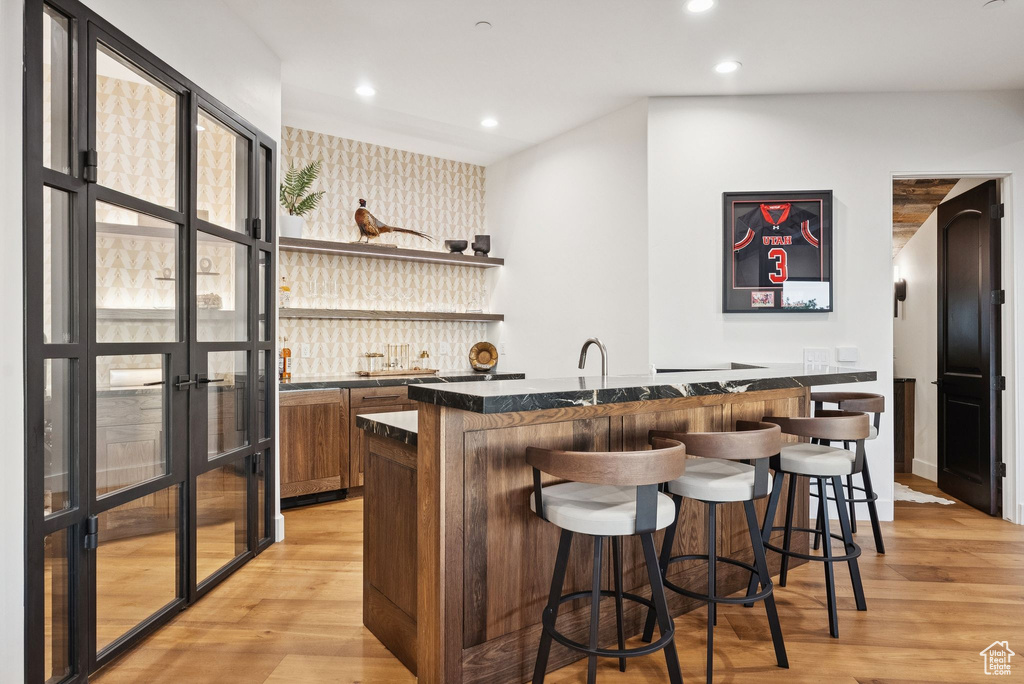 Indoor wet bar with wallpapered walls, light wood-style flooring, recessed lighting, and an accent wall