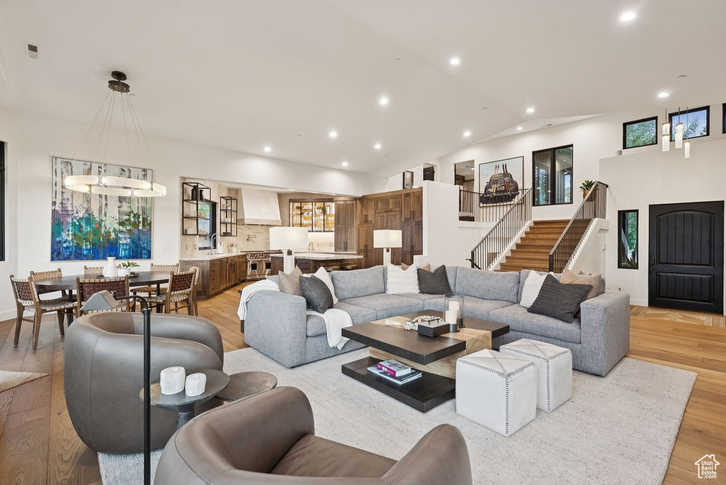 Living area with recessed lighting, light wood-style floors, lofted ceiling, and stairway