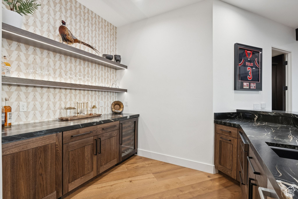 Indoor wet bar featuring light wood-style floors, backsplash, and beverage cooler