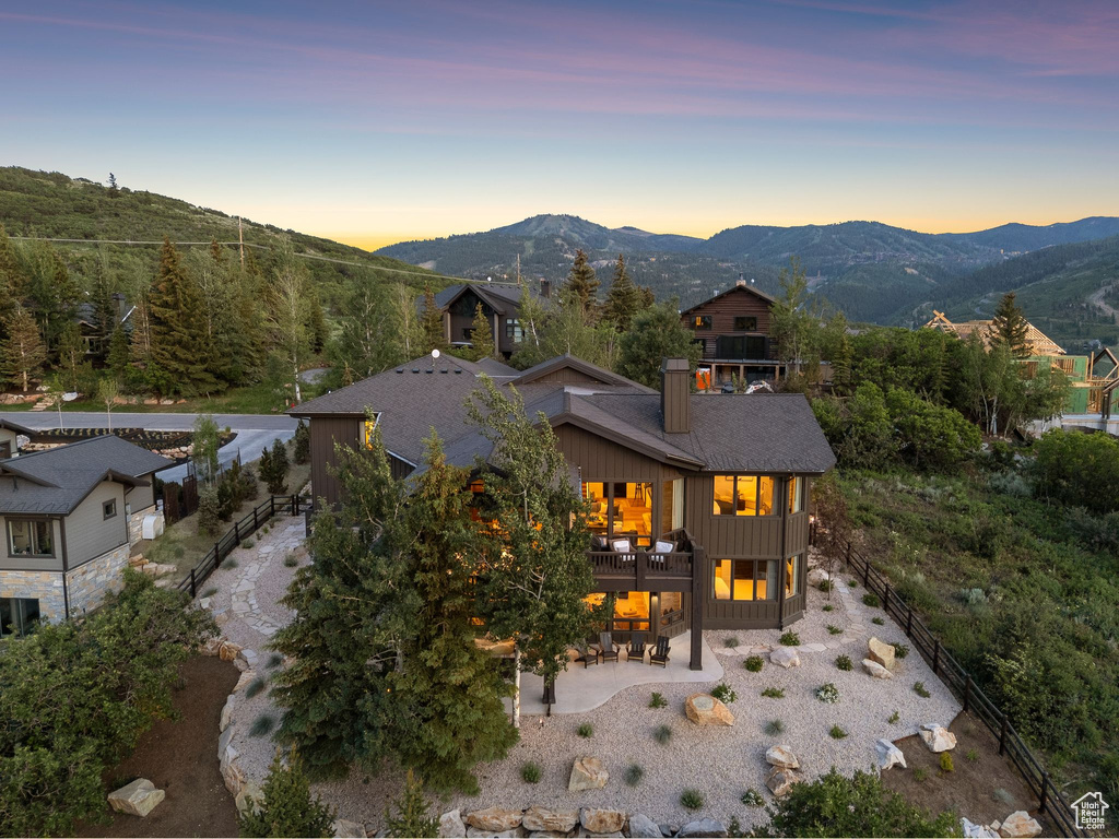 Back of property at dusk featuring a patio area, a balcony, a mountain view, board and batten siding, and a chimney