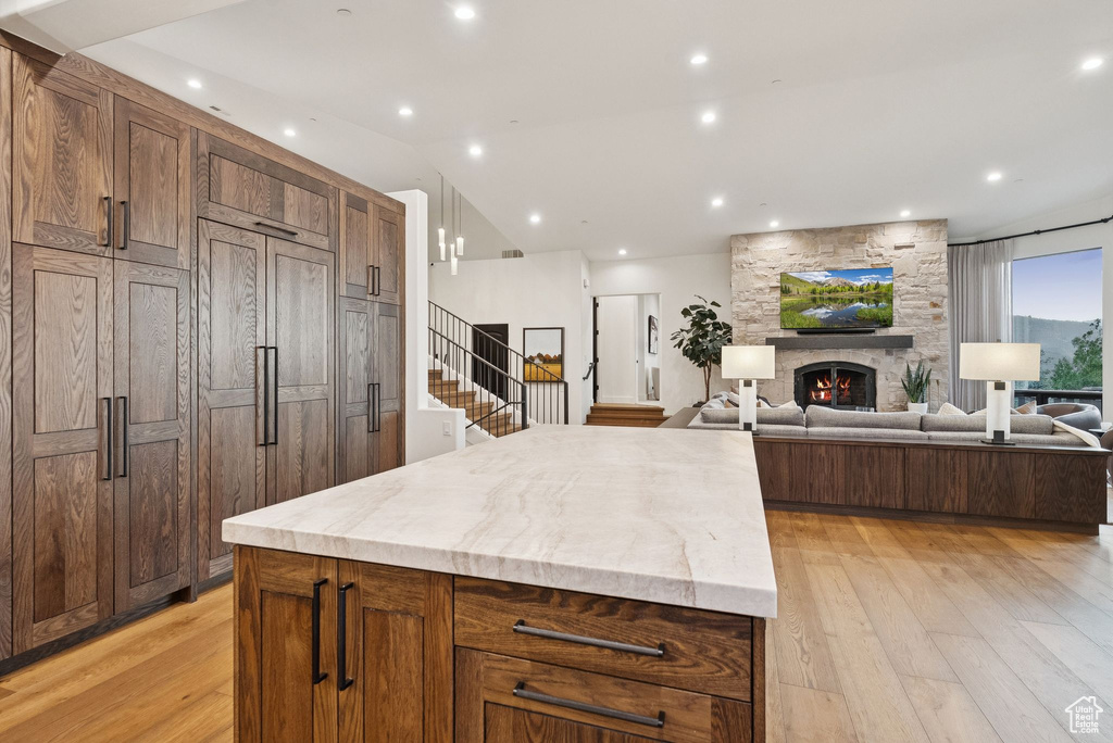 Kitchen with light wood-type flooring, a center island, a fireplace, vaulted ceiling, and light stone countertops