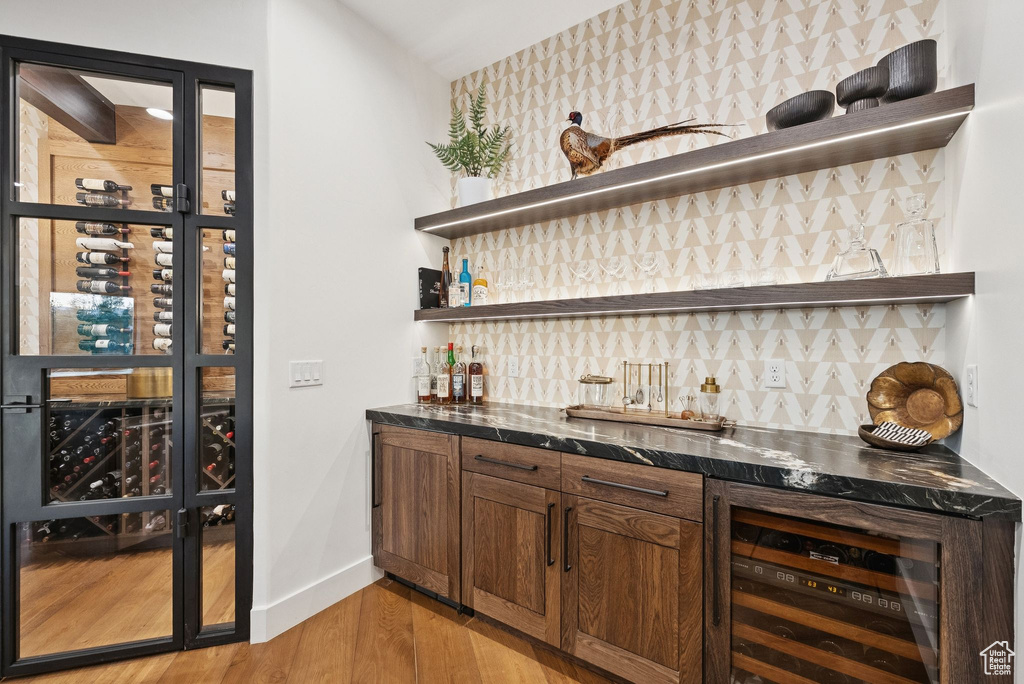Indoor wet bar with beverage cooler, light wood-style flooring, and backsplash