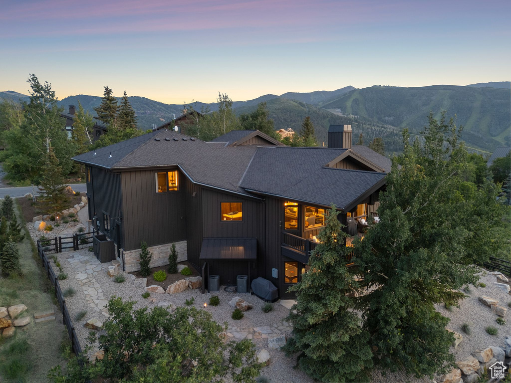 Back of house at dusk featuring a mountain view, roof with shingles, and stone siding