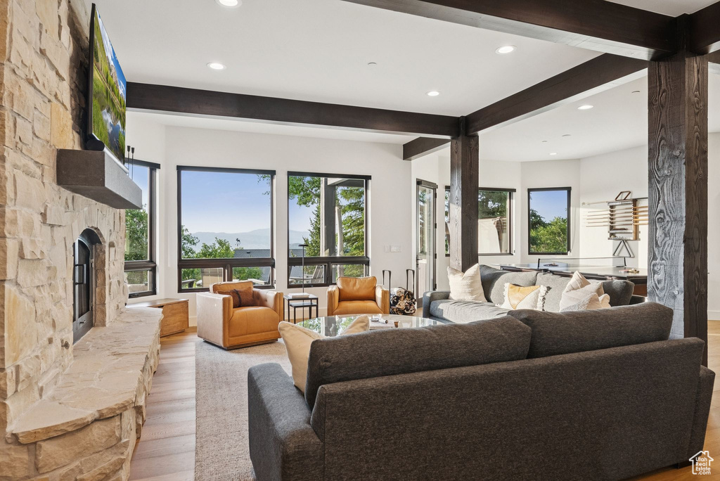 Living area featuring beamed ceiling, light wood-style flooring, plenty of natural light, recessed lighting, and a stone fireplace