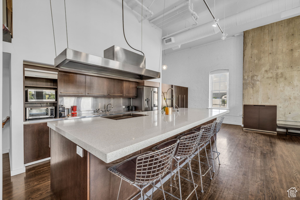 Kitchen featuring wall chimney exhaust hood, dark wood-style floors, a towering ceiling, stainless steel appliances, and modern cabinets