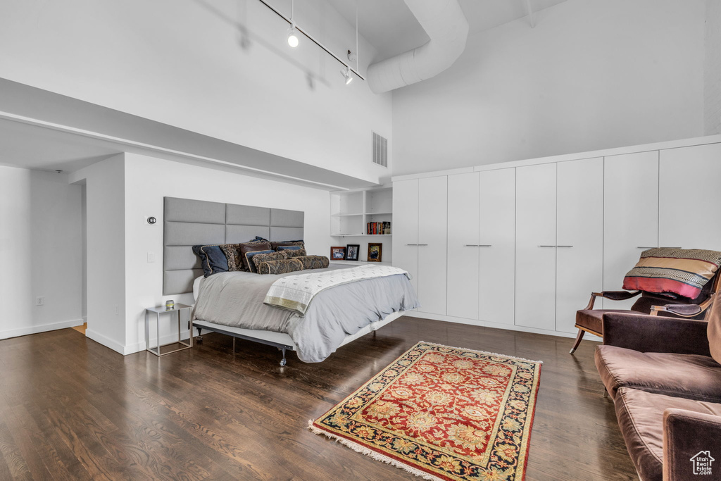 Bedroom with a towering ceiling, wood finished floors, and track lighting