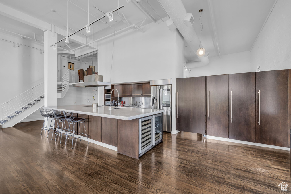 Kitchen with stainless steel refrigerator with ice dispenser, light countertops, dark wood-type flooring, a breakfast bar area, and track lighting