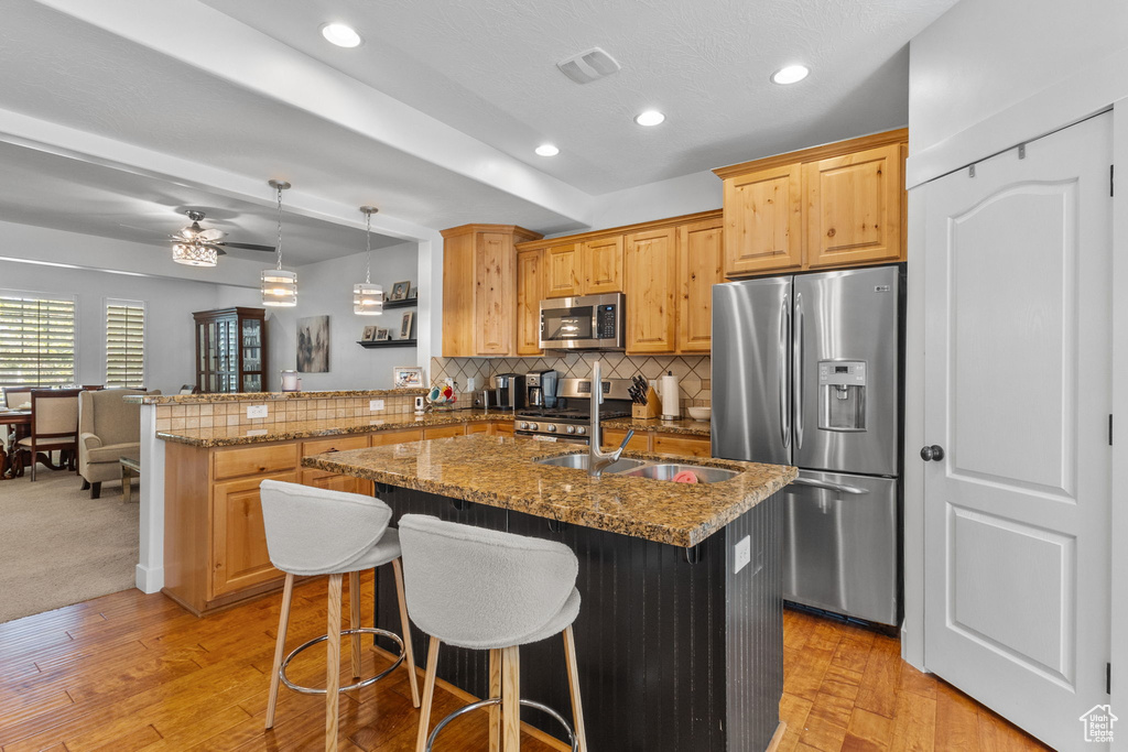 Kitchen featuring appliances with stainless steel finishes, a peninsula, decorative backsplash, light wood-style flooring, and stone counters