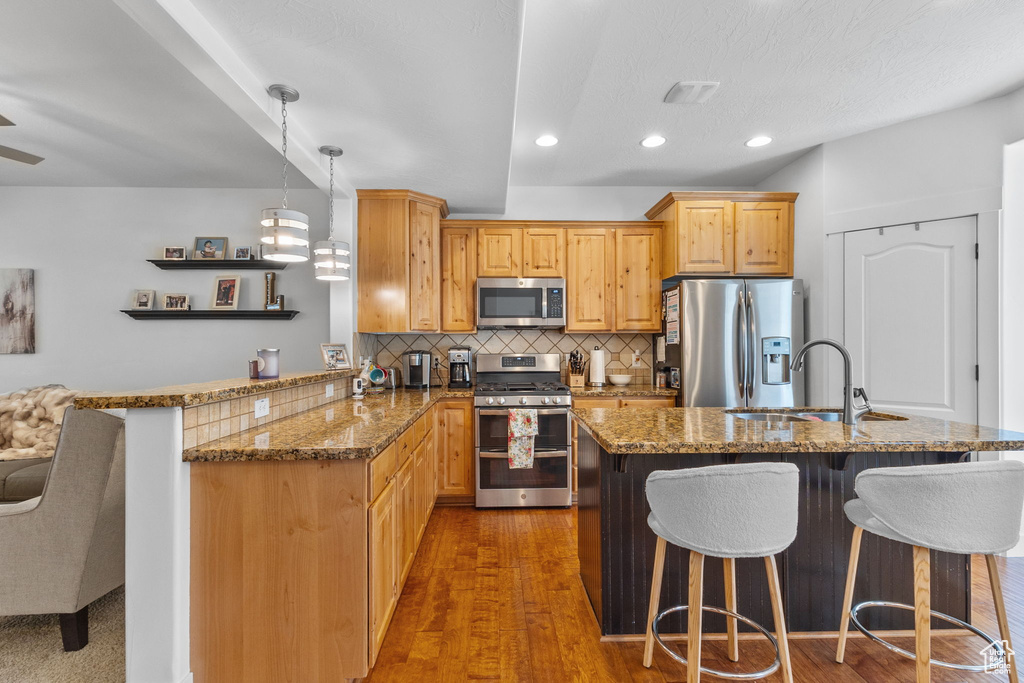 Kitchen featuring stainless steel appliances, a kitchen breakfast bar, stone countertops, a peninsula, and backsplash