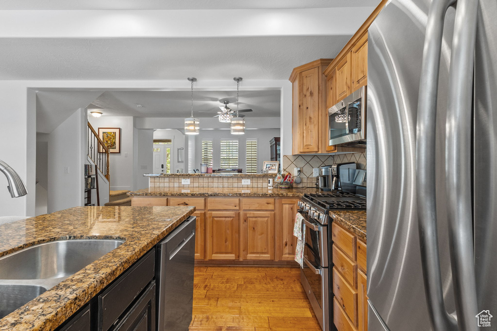 Kitchen featuring stainless steel appliances, light wood-style flooring, decorative backsplash, a ceiling fan, and decorative light fixtures
