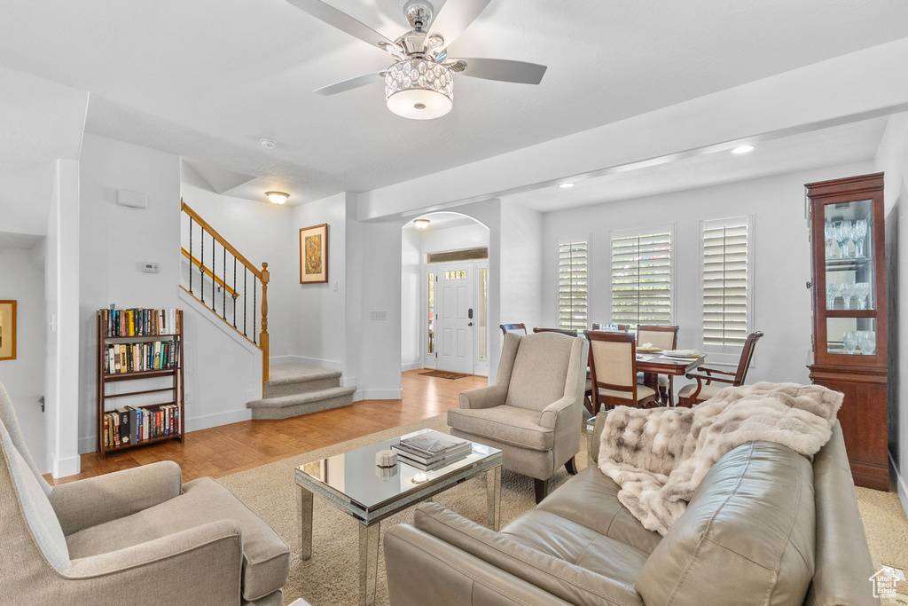Living area featuring arched walkways, light wood finished floors, stairway, ceiling fan, and recessed lighting