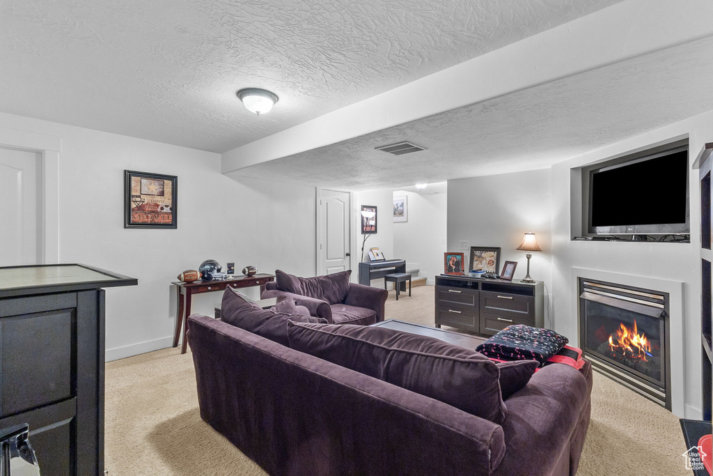 Living area with light colored carpet, a warm lit fireplace, and a textured ceiling