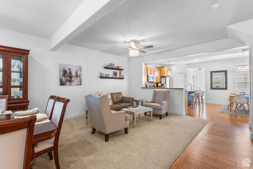 Living area with light wood finished floors, a ceiling fan, and beam ceiling