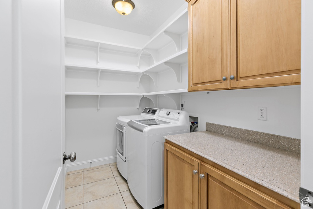 Washroom with washer and clothes dryer, cabinet space, and light tile patterned floors