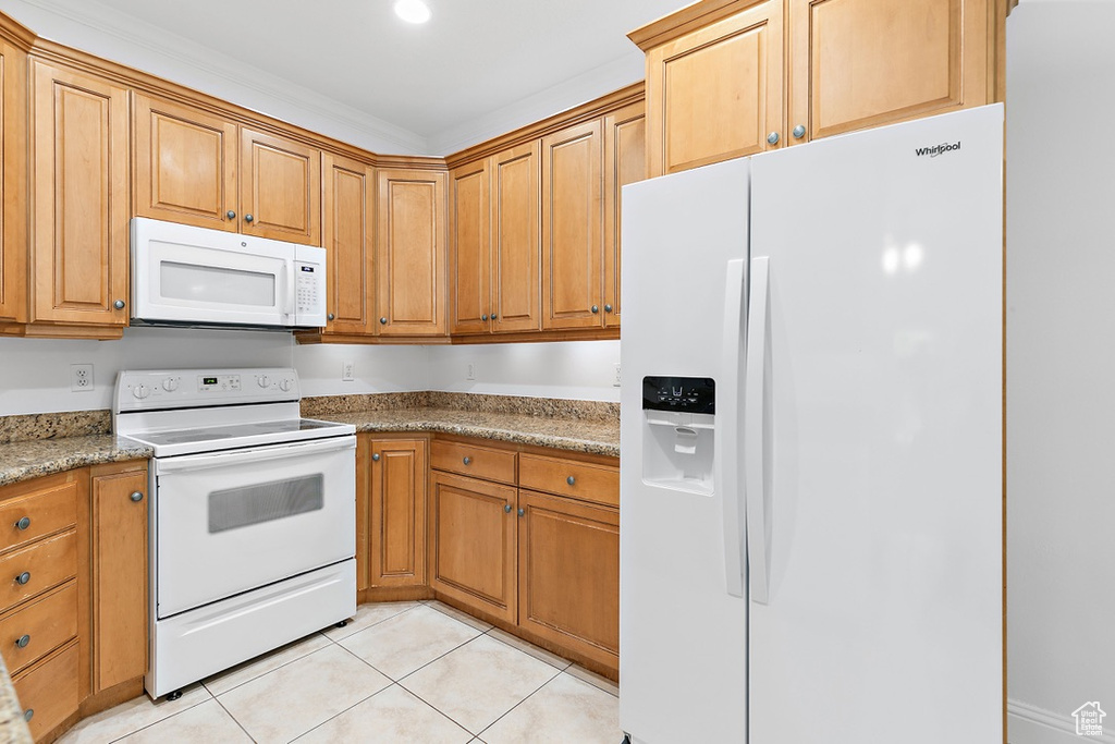 Kitchen with white appliances, light tile patterned floors, and brown cabinets