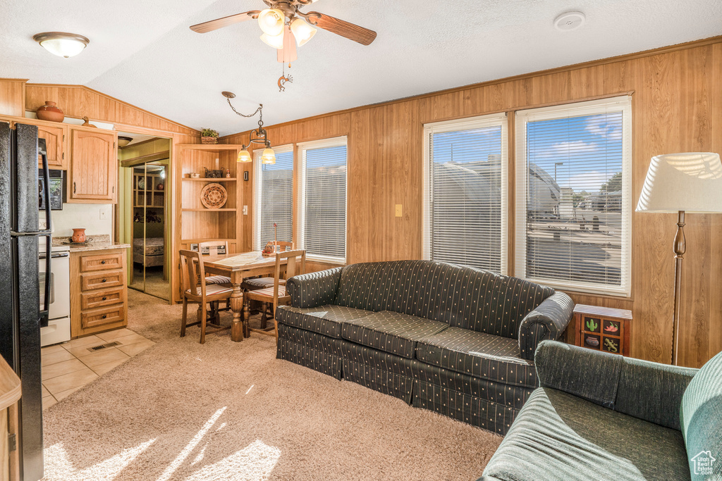 Living room with wooden walls, vaulted ceiling, healthy amount of natural light, a ceiling fan, and light tile patterned flooring