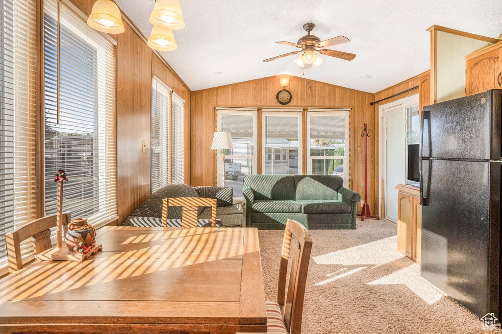 Dining space featuring lofted ceiling, wood walls, ceiling fan, and light carpet