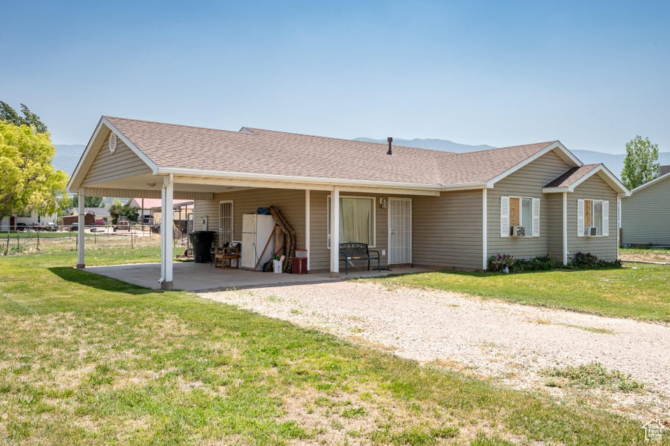 Back of property with a shingled roof, an attached carport, and gravel driveway