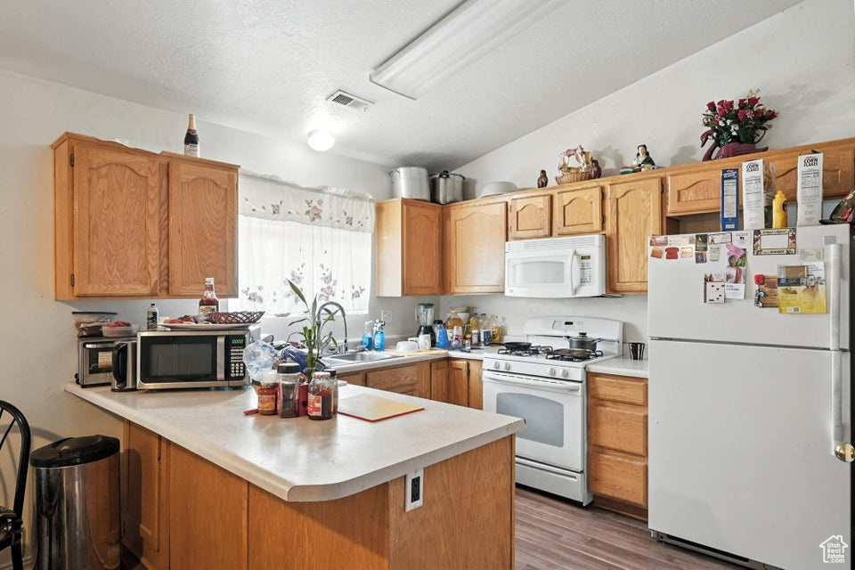 Kitchen featuring white appliances, a peninsula, light countertops, and light wood finished floors