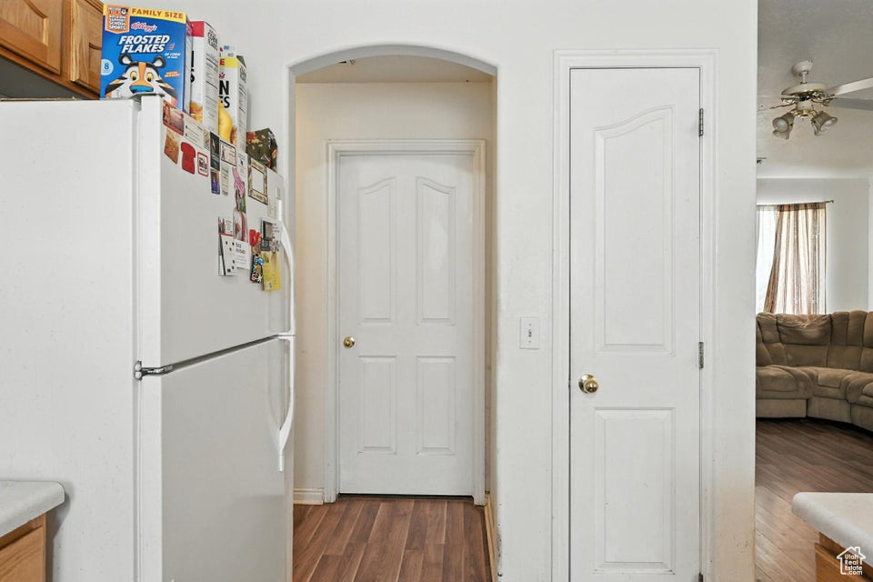 Kitchen featuring freestanding refrigerator, dark wood-style flooring, arched walkways, ceiling fan, and brown cabinetry