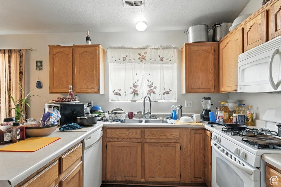 Kitchen featuring white appliances, light countertops, a textured ceiling, and brown cabinets